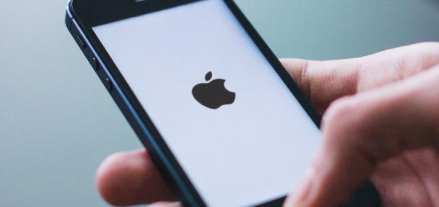 En hånd der holder en Iphone med et sort apple logo